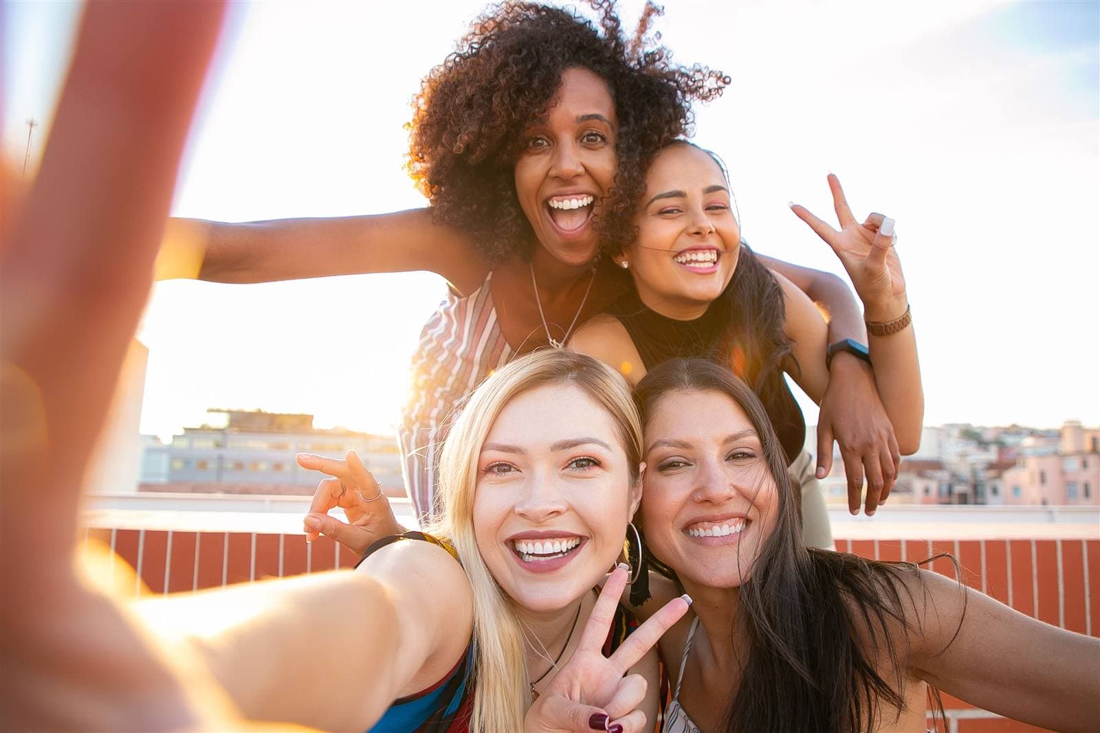 Four friends laughing in a rooftop selfie at sunset