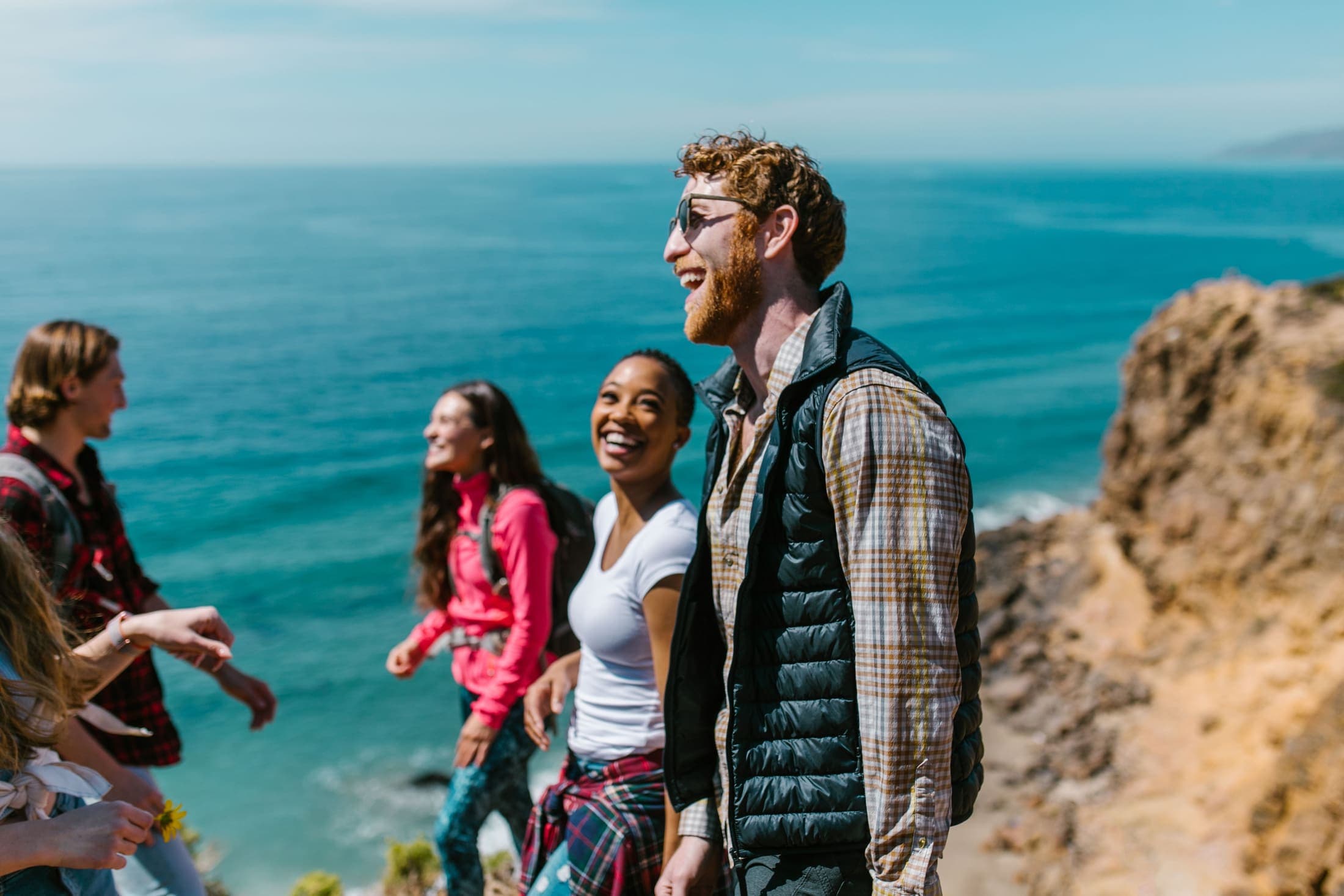 A group of friends laughing together on a coastal cliff walk